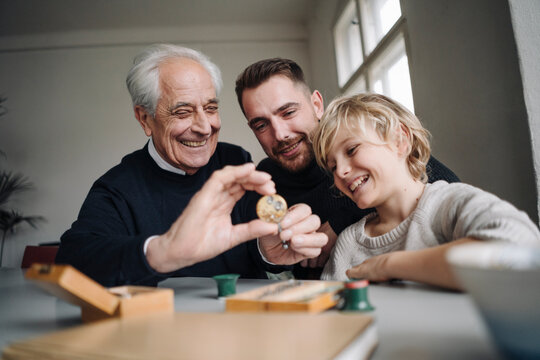 Happy watchmaker showing clockwork to young man and boy