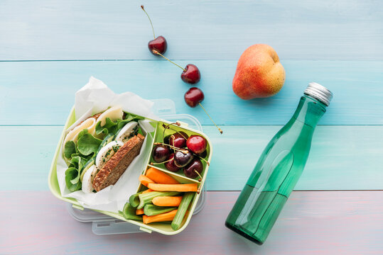 Healthy school food in a lunch box, vegetarian sandwich with cheese, lettuce, cucumber, egg and cress, sliced carrot and celery, cherries and pear