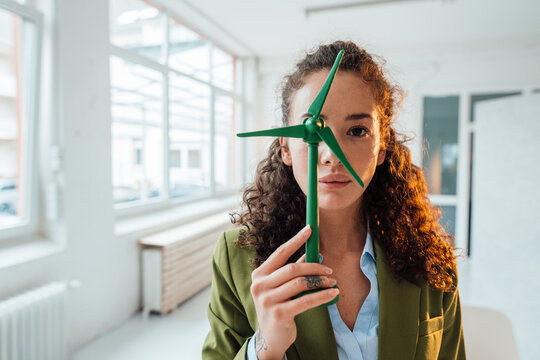 Young engineer covering eye with wind turbine model in office