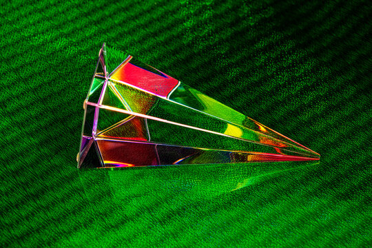 pyramidal prism refracting light with rainbow spectrum and lens flare on a textured green reflective surface