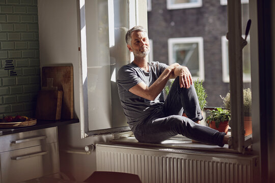 Smiling mature man sitting at the window at home