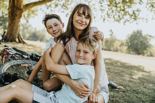 Mother embracing sons while sitting in public park