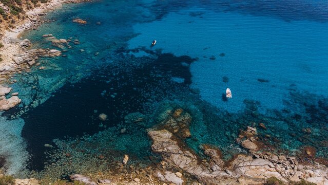 Aerial view shows a boat on turquoise water near the rocky coast