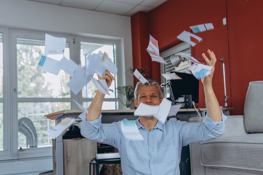 Stressed businessman throws paperwork in the office due to burnout