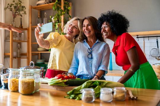 Happy multiracial women taking selfie through mobile phone in kitchen at home