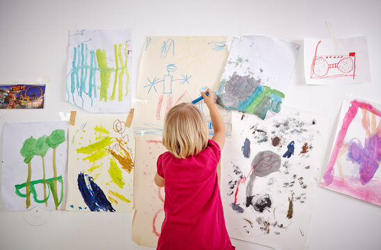 Little girl painting on wall of children's room, rear view
