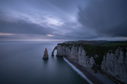 France, Normandy, Etretat, Falaise dAval cliffs and Aiguille dEtretat sea stack at cloudy dusk