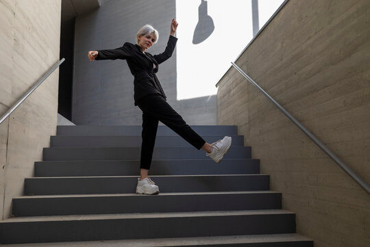 Businesswoman wearing elegant suit dancing on steps in building