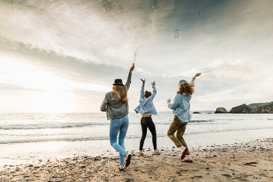 Happy friends making soap bubbles on the beach