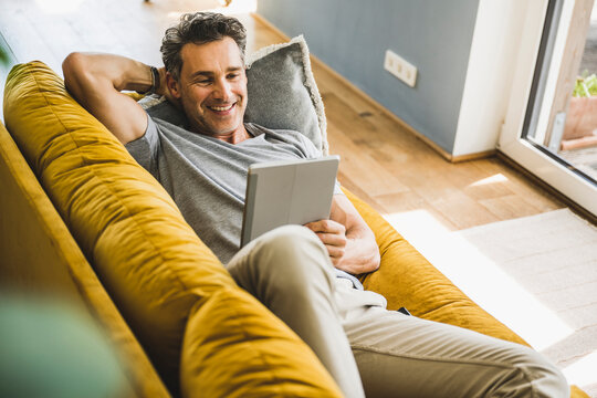 Smiling man using digital tablet while lying on sofa at home