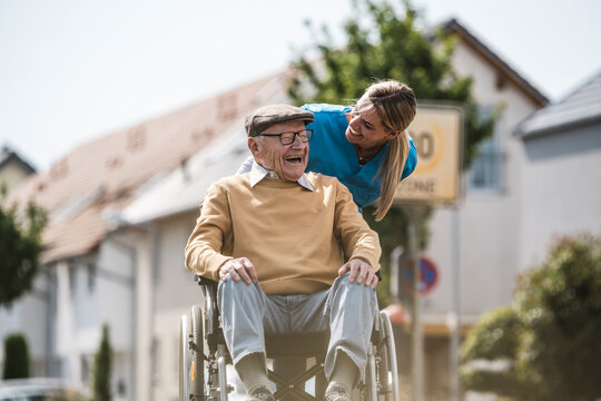Cheerful nurse talking with senior man sitting in wheelchair