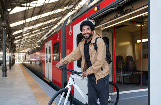 Smiling commuter disembarking with bicycle from train at station