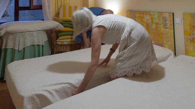 Senior Couple Making Beds Together In Cozy Twin Bedroom At Home