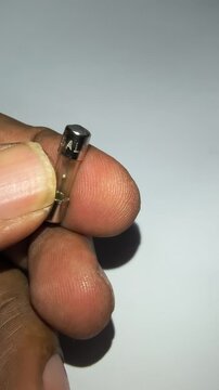 Close up of hand holding transparent 5A glass cartridge fuse for visual check.