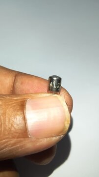 Macro shot of hand holding a 5Amp glass cartridge fuse showing stamped cap marking.