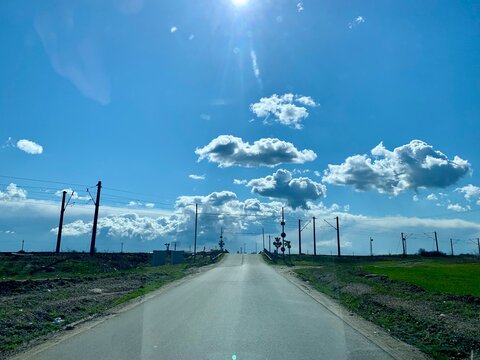 Carretera asfaltada rural que conduce hacia un paso a nivel bajo un cielo azul muy brillante