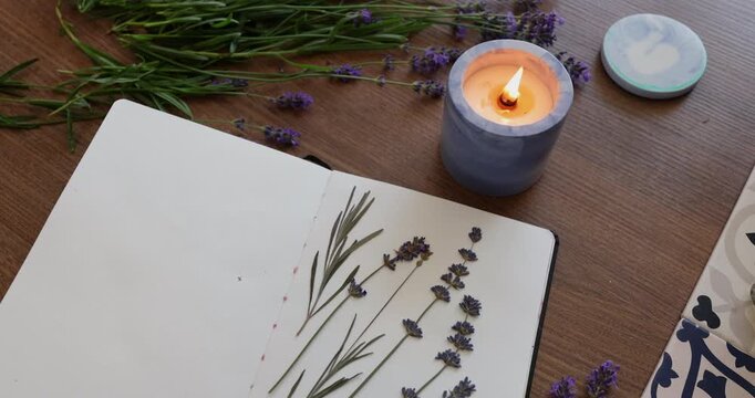 Lavender herbarium flat lay candle video. Open notebook contains dried flowers on wooden background. Creative process with burning flame and violet blossoms.
