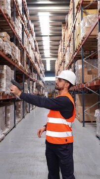Male inventory manager using a barcode scanner in a large distribution center. He is wearing a hard hat and a high visibility vest