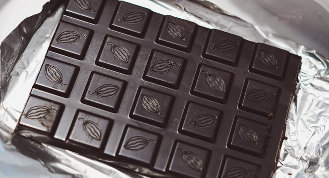 Dark chocolate bar with embossed cacao pod pattern resting on silver foil wrapper