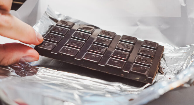 Hand lifting a dark chocolate bar with cacao pattern from silver foil wrapper