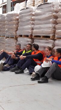 Diverse group of tired industrial workers resting on the floor. Exhausted manual laborers taking a break from work in a logistics center