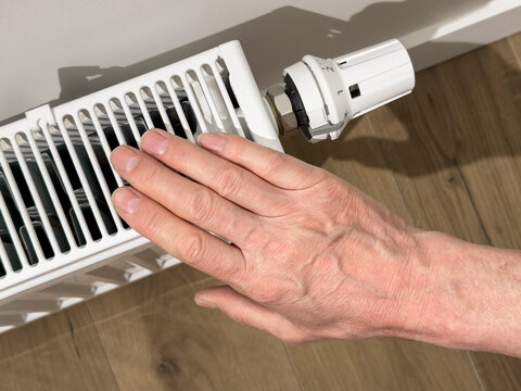 Hand adjusts a radiator thermostat in a home interior. Close up of heating control on a white valve. Energy saving maintenance for indoor temperature regulation..