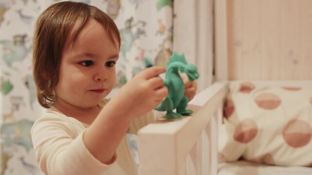3 year old girl smiling while holding a green dragon toy during creative play at home