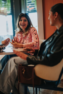 Two women chatting and laughing at a cafe table. Casual daytime conversation between friends in a warm indoor setting.