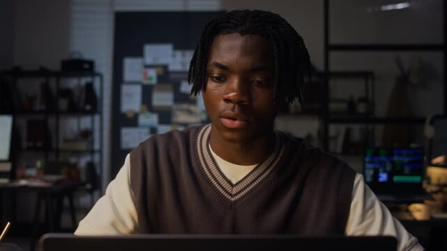 Close up of young adult African American man working late on laptop in office, rubbing face and holding head in hands from exhaustion. Footage for corporate mental health and burnout campaigns