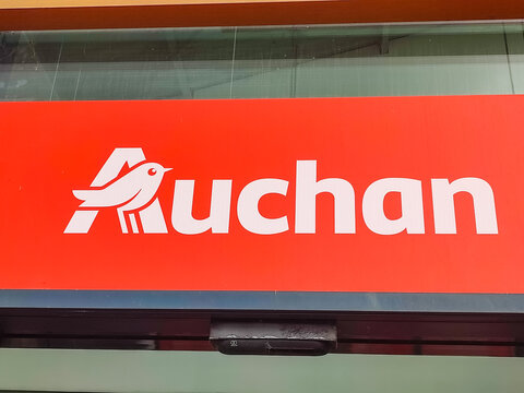 Colleville, France - June 28, 2026: Auchan supermarket logo displayed prominently on red background, featuring a stylized bird and bold lettering