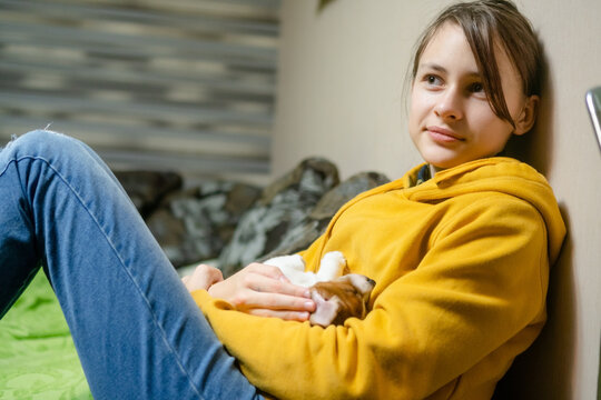 Preteen smiling and holding a fluffy puppy on the floor in a cozy room at home. Cheerful pet owner hugging and cuddling small dog with happy loving affectionate joy in natural light.