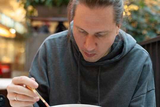 Man focusing on a bowl of food while dining at an Asian restaurant with concentrated look. Guy absorbed in his meal during a serious dining experience. Dedicated food enthusiast savoring every bite