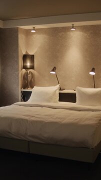 Vertical shot of empty double bed featuring linens inside modern hotel room. Clip serves well for hospitality marketing campaigns or travel agency promotions, wide shot, zoom in