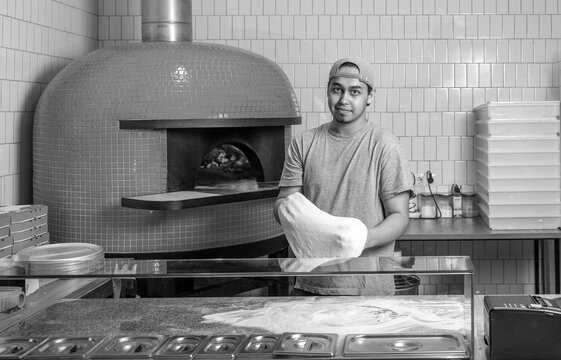 Dough for pizza rolling with hands while working in a pizza place. The process of making pizzas. Black and white