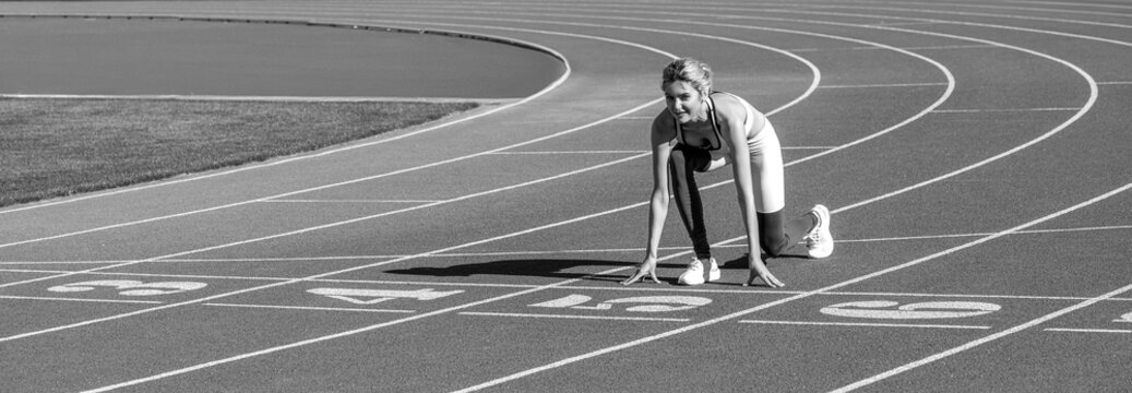 Runner woman in sportswear getting ready to run sprint at low start on stadium track. Black and white