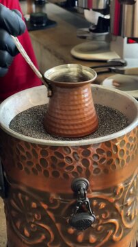Traditional Turkish coffee being prepared on hot sand in a copper cezve.