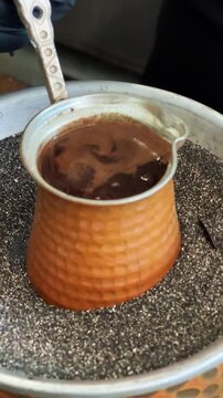 Traditional Turkish coffee being prepared on hot sand in a copper cezve.