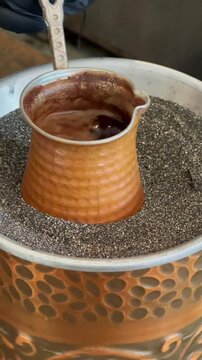 Traditional Turkish coffee being prepared on hot sand in a copper cezve.