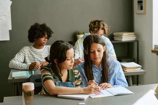Diverse teenage students studying together in classroom, reading notes and writing in notebooks, representing teamwork and learning. Ideal for school marketing and education campaigns