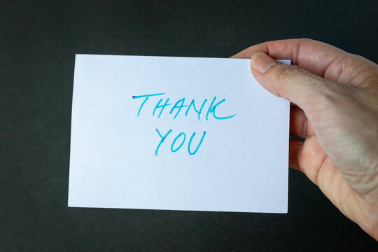 Hand holding a thank you card. Isolated on dark background.