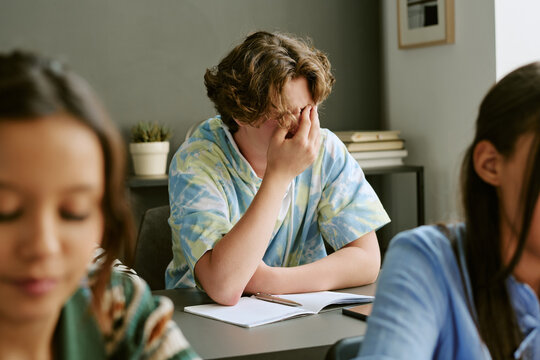 Diverse teenager students studying in classroom, central teen covering face while struggling with school stress and academic pressure. Useful for education, teen mental health campaigns