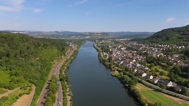 Moselle valley, Mosel river flowing past village, road and railway tracks, lush green hills and cityscape of Trier, landscape in summer, aerial view