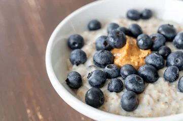 Bowl of oatmeal porridge with blueberries and peanut butter on wooden table, healthy breakfast and nutrition © molenira