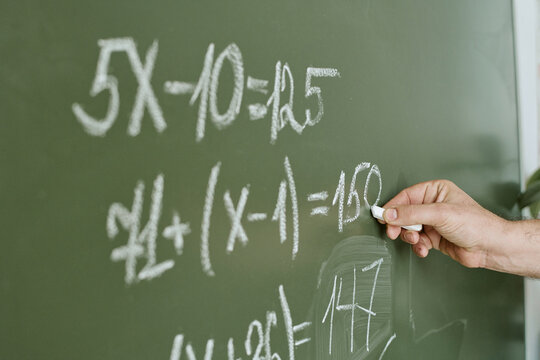 Close up of teacher hand writing algebra equations on chalkboard, explaining math lesson in classroom. Education concept for school learning, tutoring, curriculum content