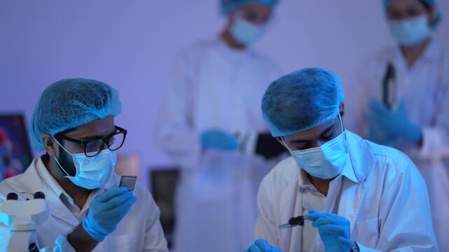 Masked scientists handle pipettes and sample tubes under dramatic blue light while colleagues collaborate in the background.