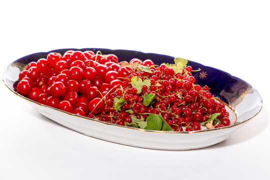 Ripe red currants and cherries on a large plate against a white background