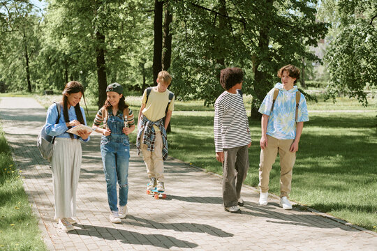 Wide shot of diverse teenage students walking and talking in sunny park, representing teamwork and learning. Ideal for education marketing, youth programs, campus promotion