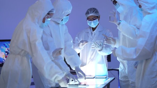 Scientists in protective suits gather around an illuminated table inspecting a wafer disc under dramatic blue cleanroom light.
