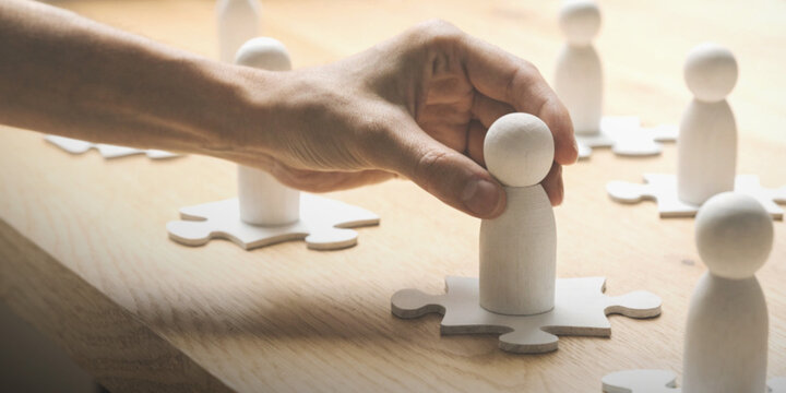 Teamwork along with planning and organizational growth with a hand holding a wooden figure on a piece of a jigsaw puzzle