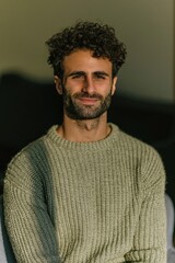 Fototapeta premium Smiling man with curly hair and knit sweater indoor portrait for lifestyle headshot and social media profile
